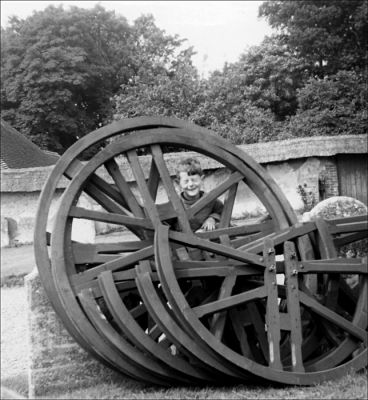 05_1CR003_16_04
Young David Holmes (aged 8) - son of Paul Holmes - later to become Bell Captain - with wheels from the tower. Note the rare thatched chalk wall in the background with a door through to Lywoods Farm (Court Farm) next door. Sadly, the wall is no longer there. 

From Paul Holmes
