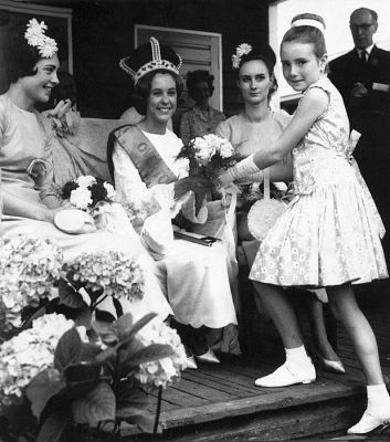 15_1OC002_03_02
Flowers being presented to the Carnival Queen in the 1960's. The man in the background is Solly Kersley who I believe played a major role in organizing the carnivals for several years. The Queen's attendant on the right is Eve Etheridge. The young girl presenting the flowers is Janice Stott. This took place on the veranda at Overton School, Lordsfield, when it was still housed in ex-army huts. 

Photo from Janice Stott
