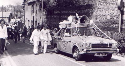 15_1OC002_03_06
This is the carnival procession coming up Kingsclere Road to the crossroads. Stan Stott, Janice's dad is driving the car with a PA system and her mum, Penny, is in the front passenger seat. The lady walking opposite is Christine Cowmeadow. 

Photo from Janice Stott
